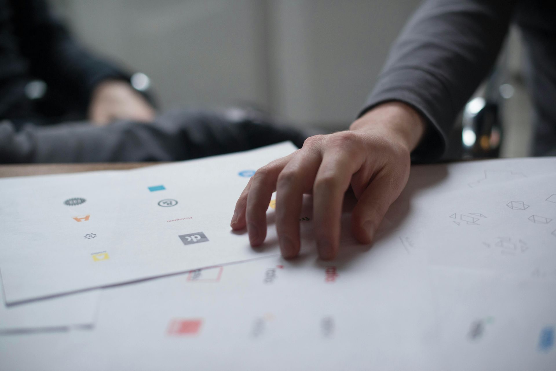 Person's hand over logo designs on paper; selecting or evaluating options.