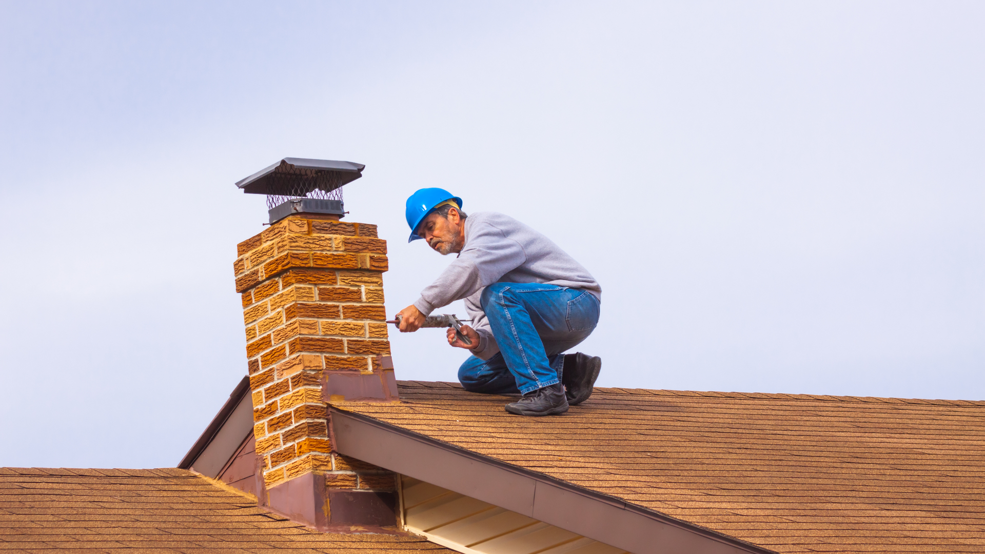 A man is kneeling on top of a roof fixing a chimney.