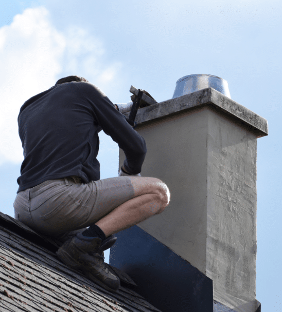 A man squatting on top of a roof next to a chimney