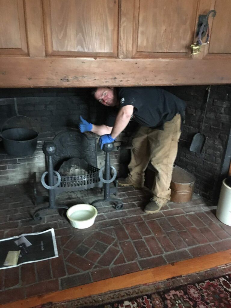 A man is standing in a fireplace cleaning it.