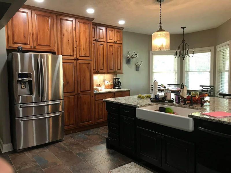 Kitchen with stainless steel refrigerator, dark wood cabinets, and black island with a white farmhouse sink.