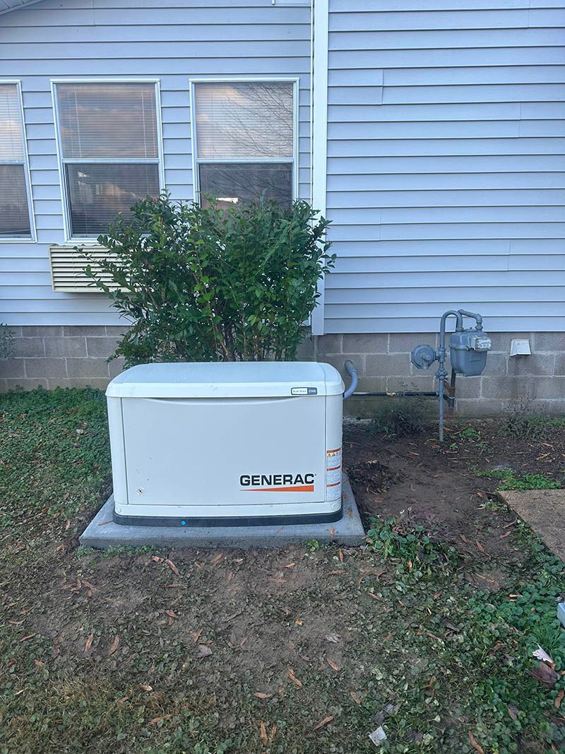 A Generac generator outside a house near a gas meter and a small bush.