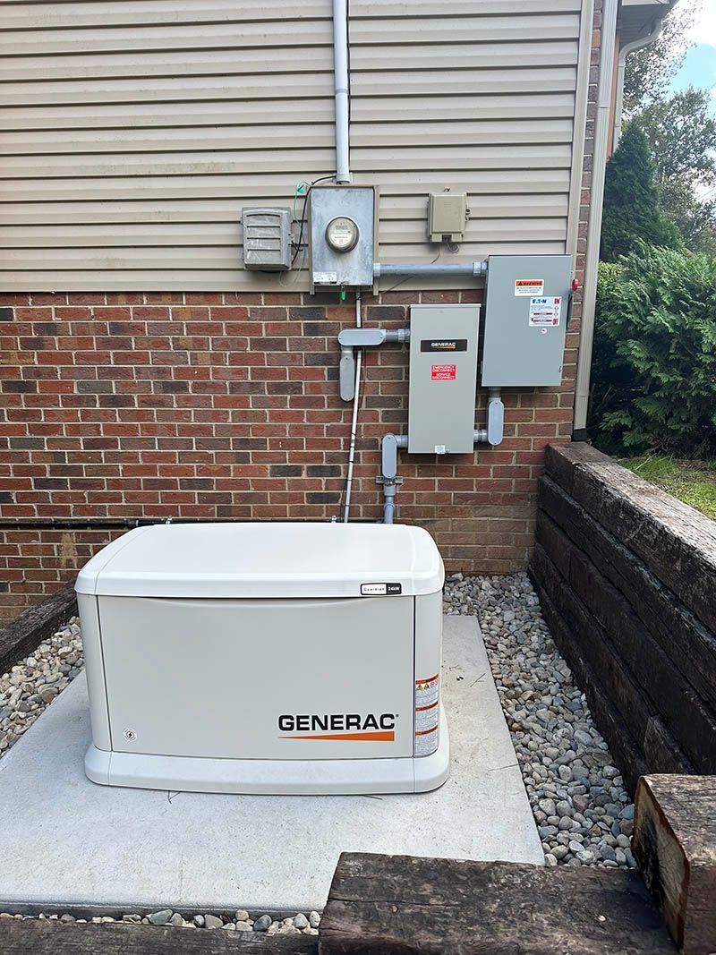 A white Generac generator on a concrete pad next to a brick and siding wall with electrical components.