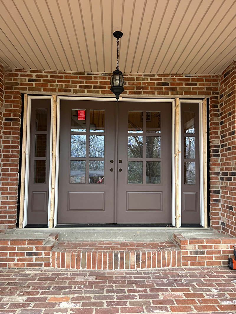 Brown double doors with glass panes, flanked by sidelights. Brick exterior, covered porch.