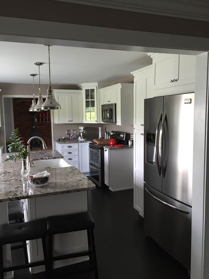Modern kitchen with white cabinets, stainless steel refrigerator, dark floor, and granite island with stools.