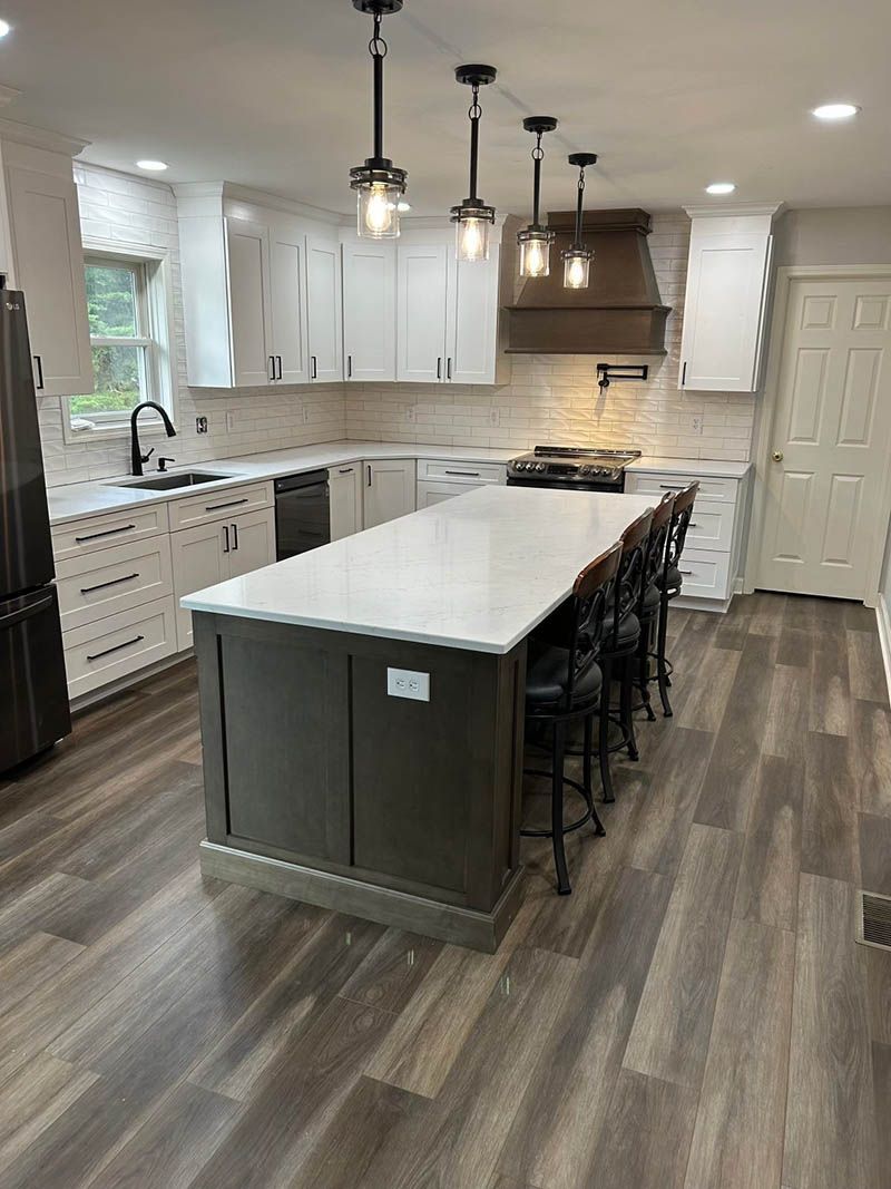Modern kitchen with white cabinets, large island with seating, pendant lights, and wood-look flooring.