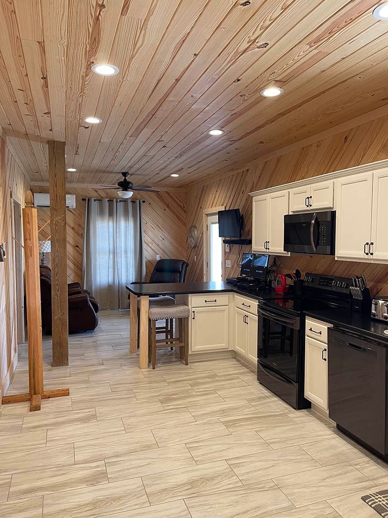 Kitchen with wood panel walls and ceiling, white cabinets, black appliances, and a central island.
