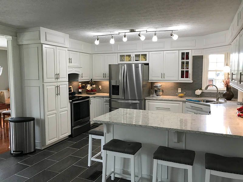 White kitchen with granite countertops, stainless steel appliances, dark tile floor, and a breakfast bar with stools.