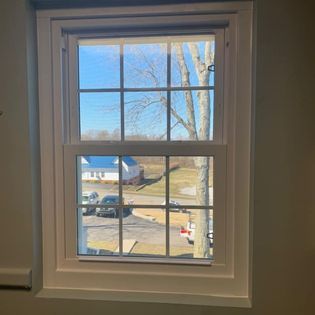 White-framed window looking out to a blue sky, house, cars, and a bare tree.