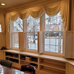 Three windows with draped valances, shutters, and built-in shelving overlooking a street.