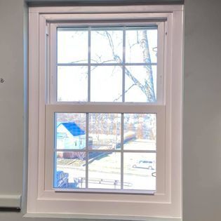 White-framed, multi-pane double-hung window with view of trees, houses, and cars; bright sunlight.