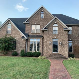 Brick house with dark roof and red brick pathway leading to the front door.