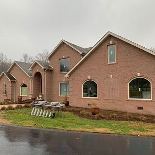 Brick house with multiple gables and arched windows; ladder on the front lawn.