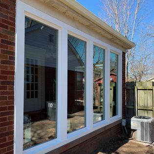 Exterior view of four connected white-framed windows on a brick building, reflecting the surrounding yard.