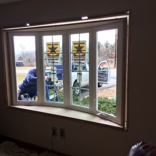Bay window installation: Workers inside, outside. White truck, trees visible. Light brown trim.