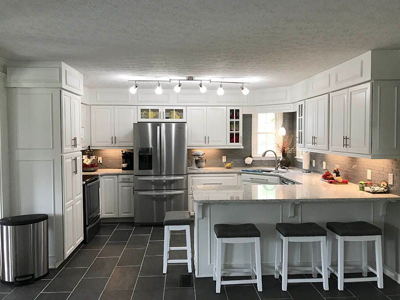White kitchen with stainless steel appliances, white cabinets, gray tile floor, and a breakfast bar with stools.