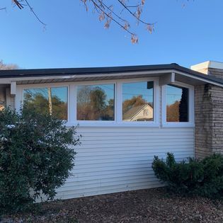 Exterior view of a house with white siding and windows reflecting trees.