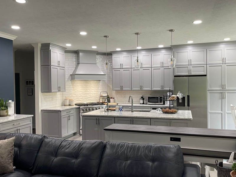 Modern gray kitchen with island, range hood, white countertops, and recessed lighting.