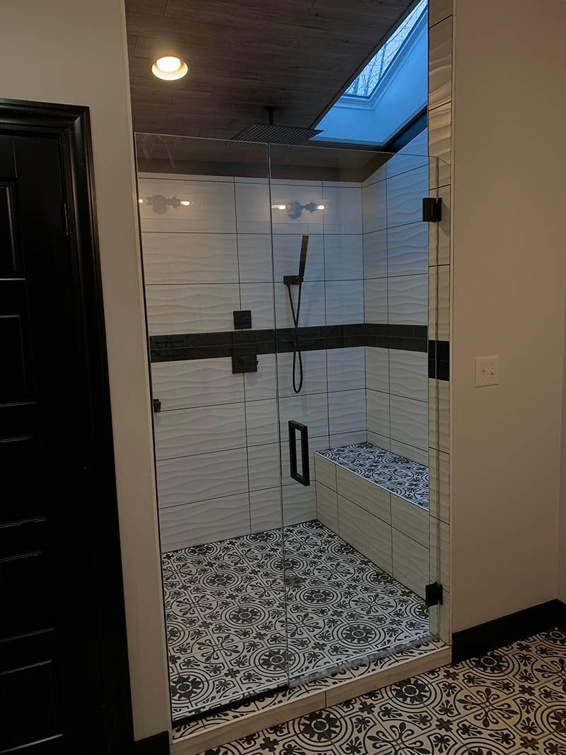 Modern shower with glass door, white and black tile, bench, and overhead skylight.