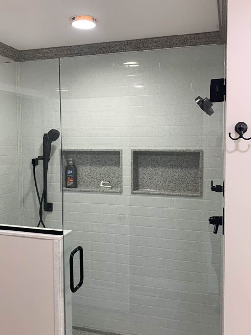 Shower with glass door, gray tile, black fixtures, and built-in niches for storage.