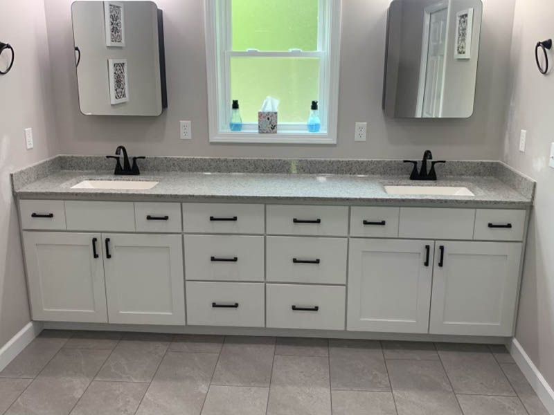 Bathroom with white cabinets, gray countertop, black faucets, and rectangular mirrors.