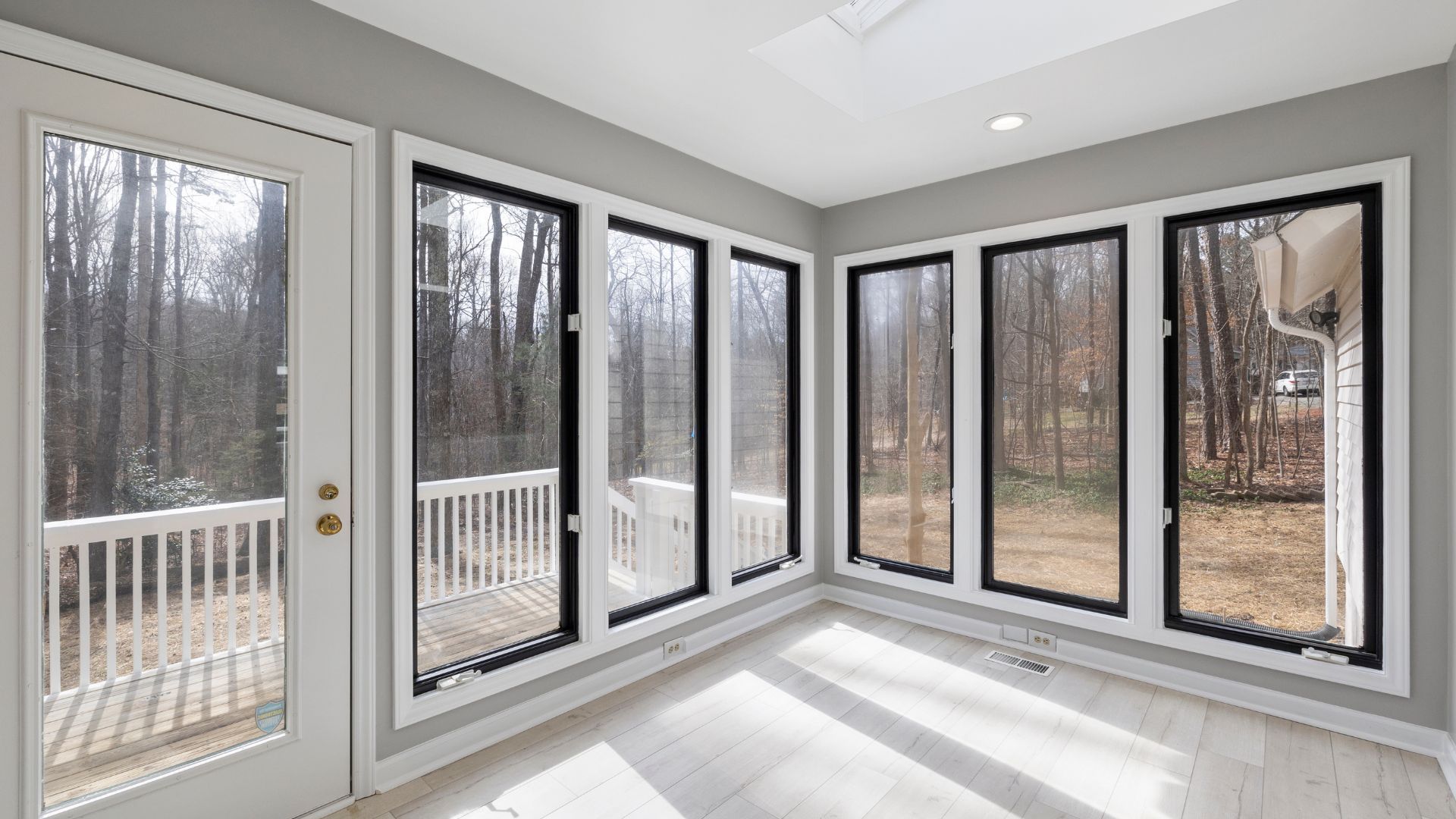 Sunroom with large windows, door to a deck, and a view of trees. White trim, black window frames.