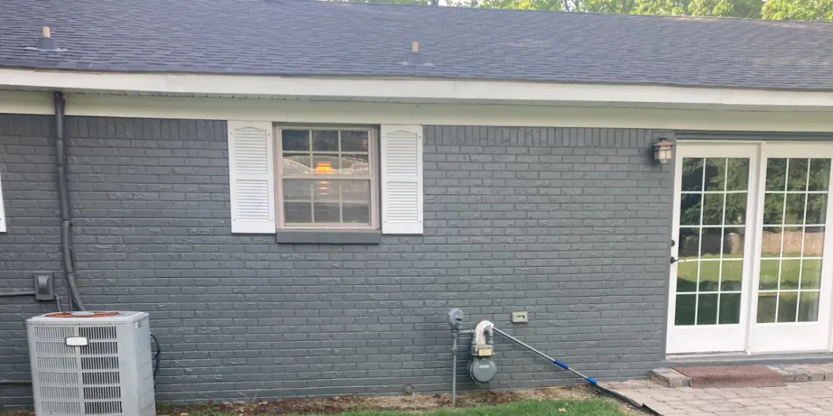Gray brick exterior of a house with white trim, window, and glass door.