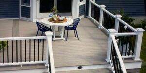 Deck with white railing, black spindles, a table and chairs. Door and house siding in the background.