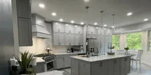 Gray and white kitchen with island, cabinets, appliances, and a table with a view of greenery through a large window.