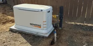 A Generac generator on a concrete pad near a wooden fence.