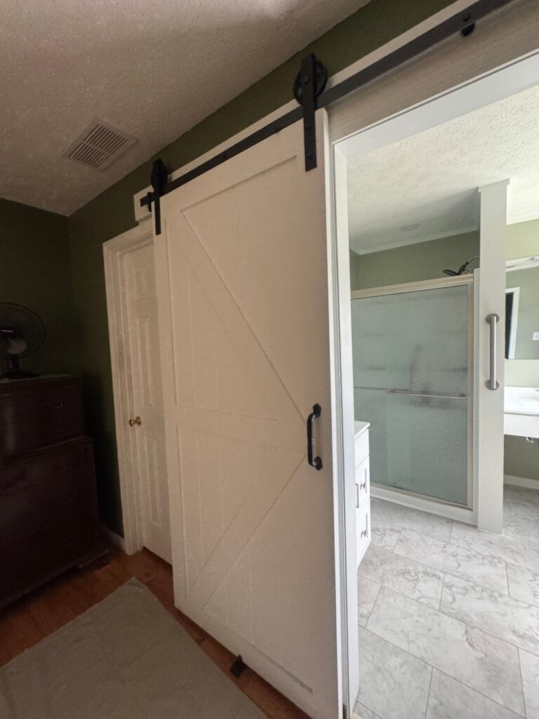 White barn door on a black track slides open to a bathroom with a shower and sink.