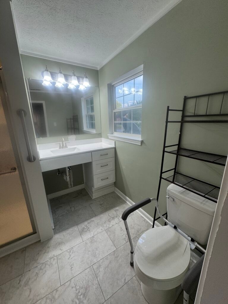 Bathroom with accessible features: vanity, grab bar, raised toilet, and shelving unit.