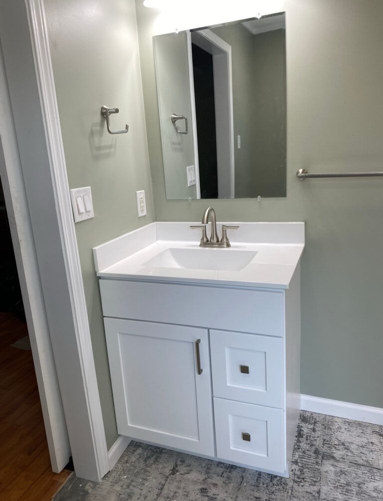 White bathroom vanity with sink, mirror, and towel rack against a green wall.
