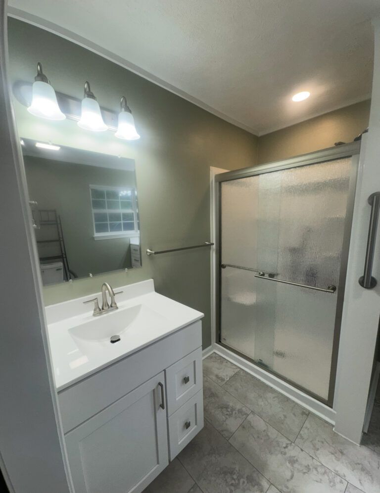 Bathroom with white vanity, frosted glass shower, and olive green walls.