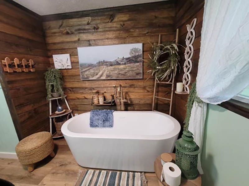 Bathroom with a white freestanding tub against a wooden plank wall, decorated with plants and decor.