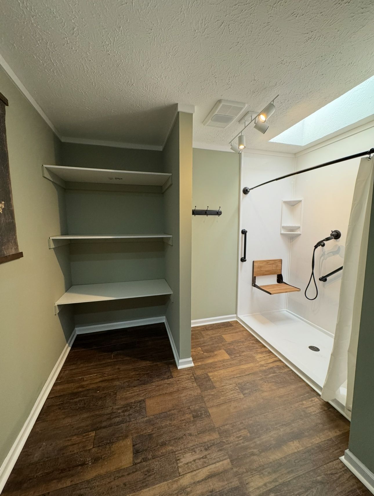 Bathroom with accessible shower, shelves, and wood-look flooring. Light green walls, white shower with built-in seat, and skylight.