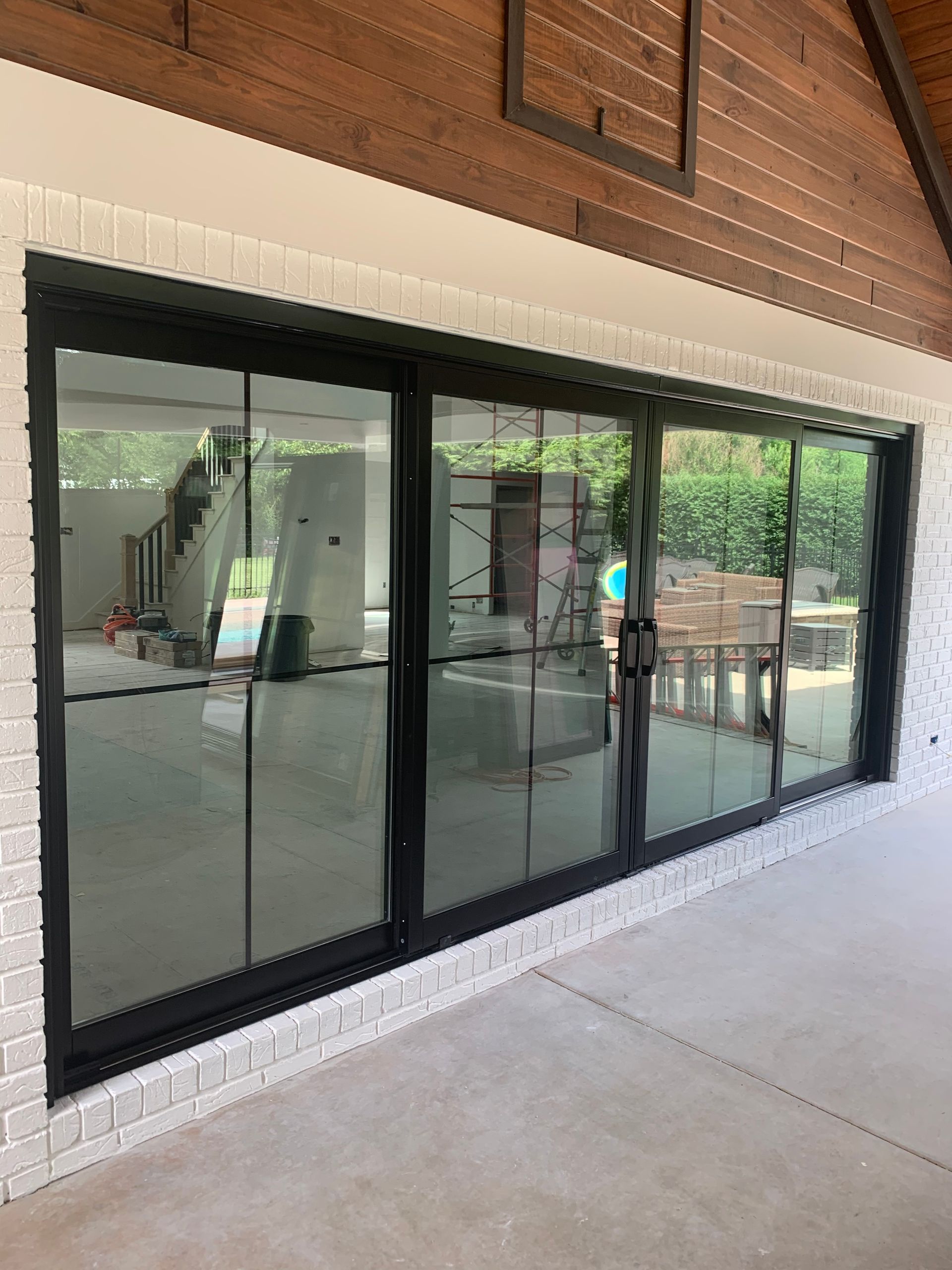 Black-framed sliding glass doors on white brick exterior. The interior shows stairs and construction.
