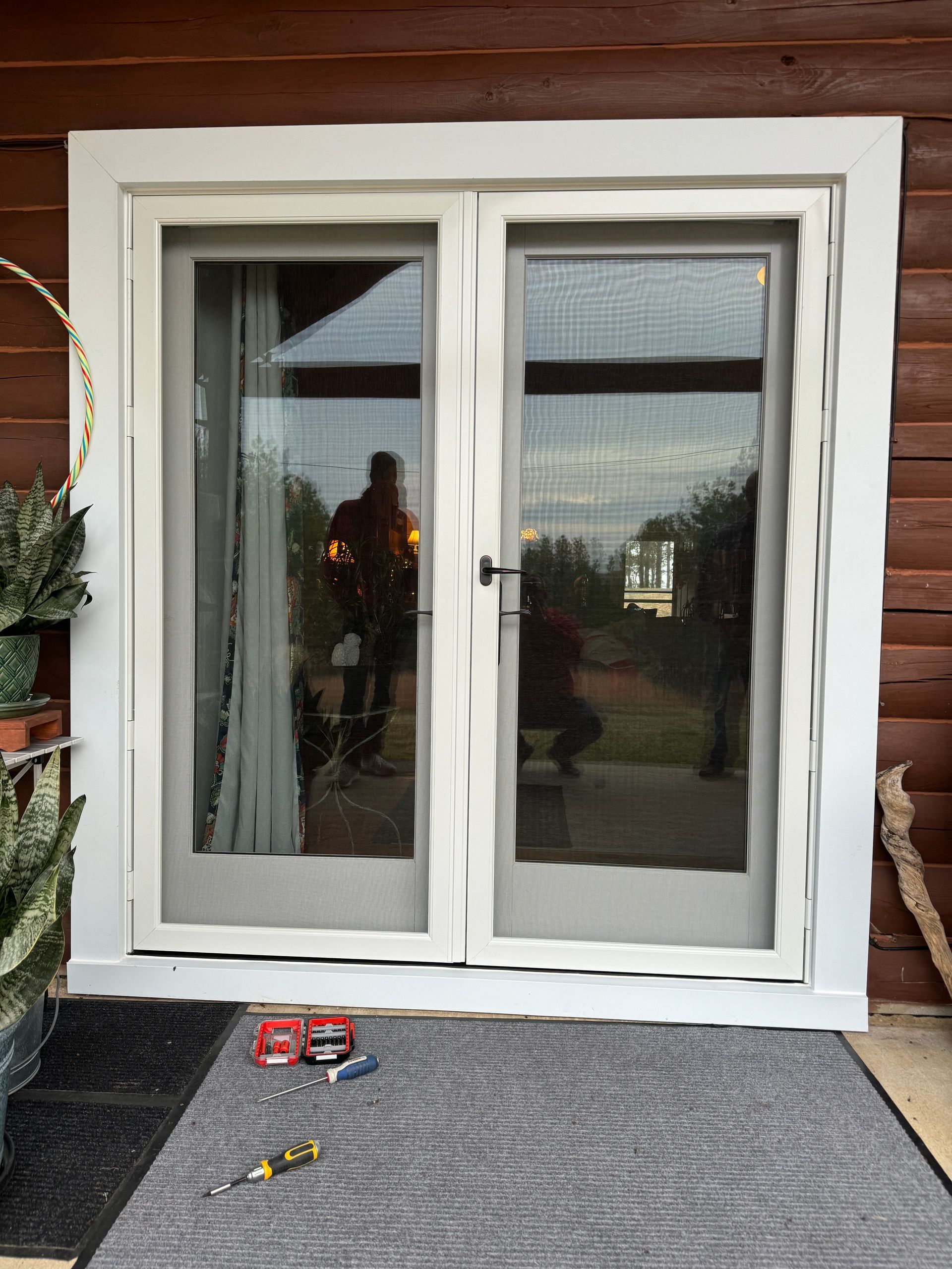Double glass doors with textured glass, black handle. Reflection of a person and a view outside. Gray rug.