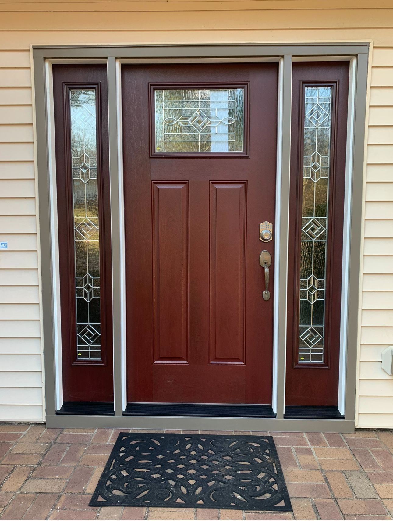 Maroon front door with sidelights, decorative glass, black doormat, brick entryway.
