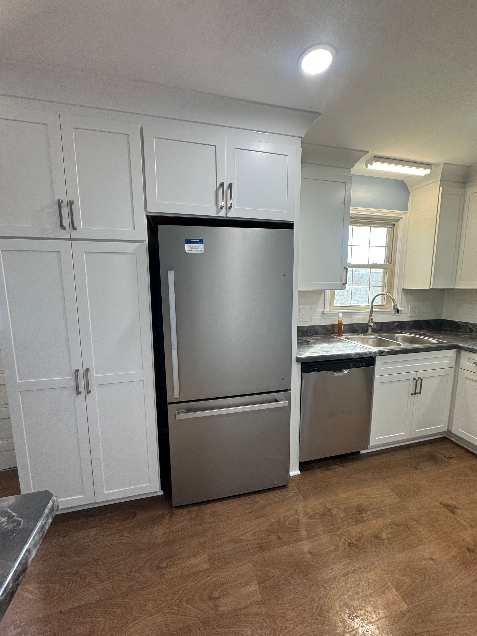 Kitchen with white cabinets, stainless steel appliances, and wood-look flooring.