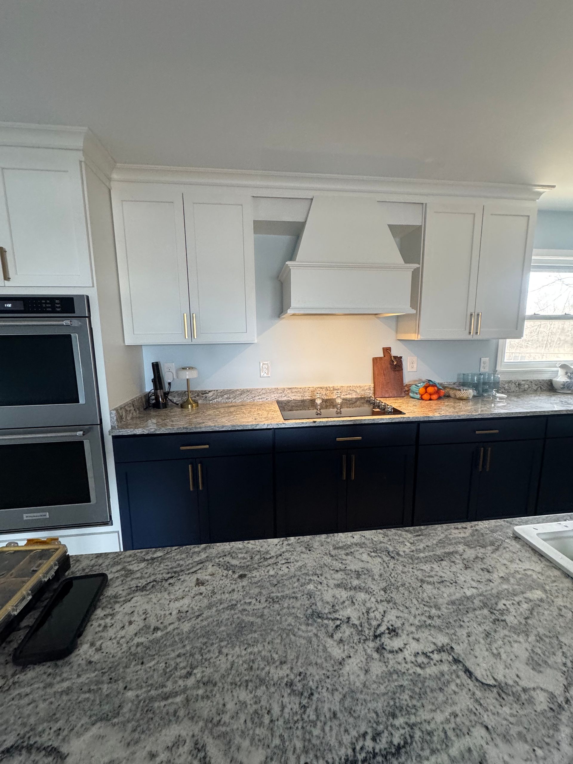 Two-toned kitchen with navy blue lower cabinets, white upper cabinets, and a white range hood. Granite countertops.