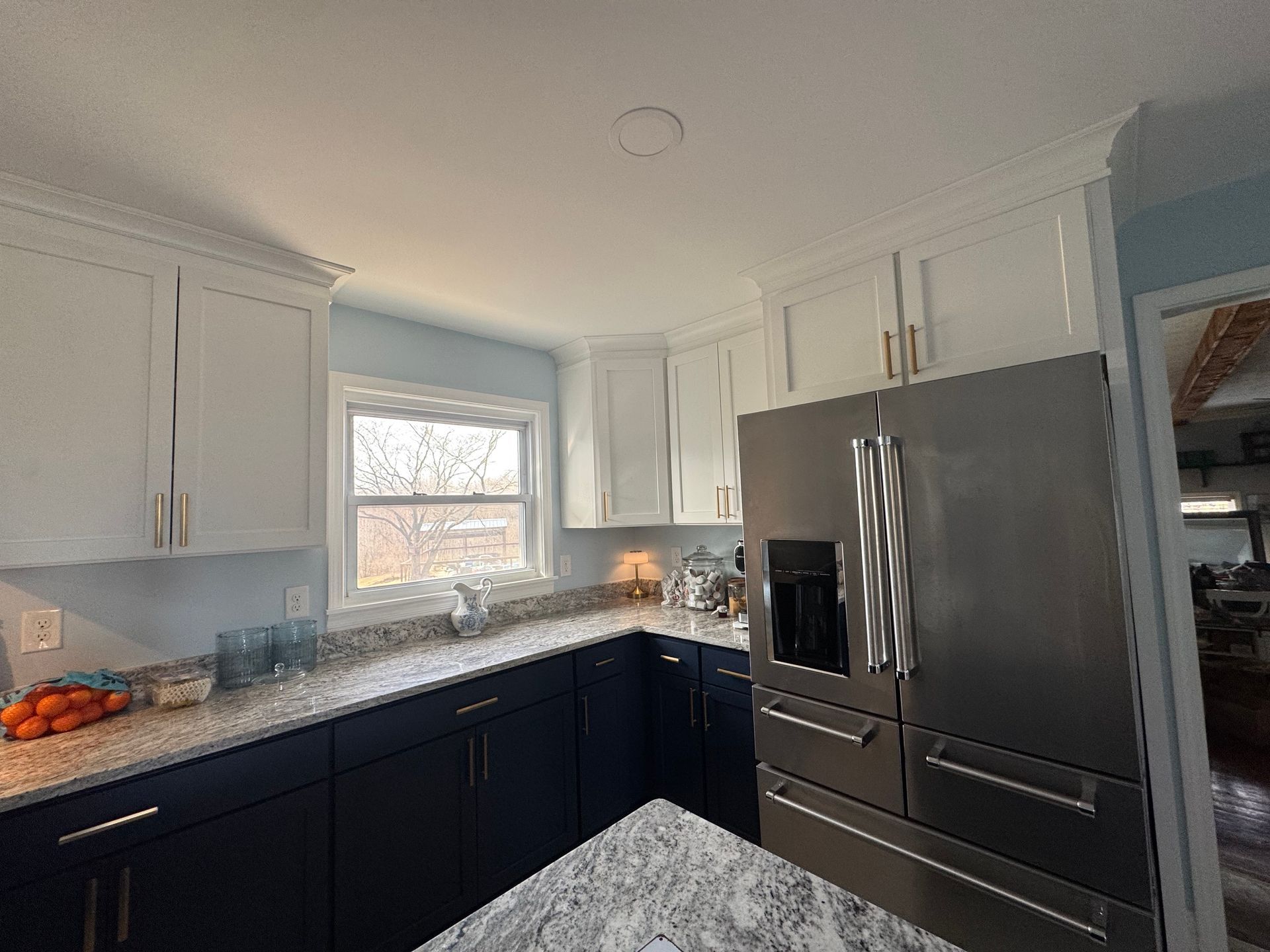 Kitchen with white upper cabinets, navy blue lower cabinets, and stainless steel refrigerator.