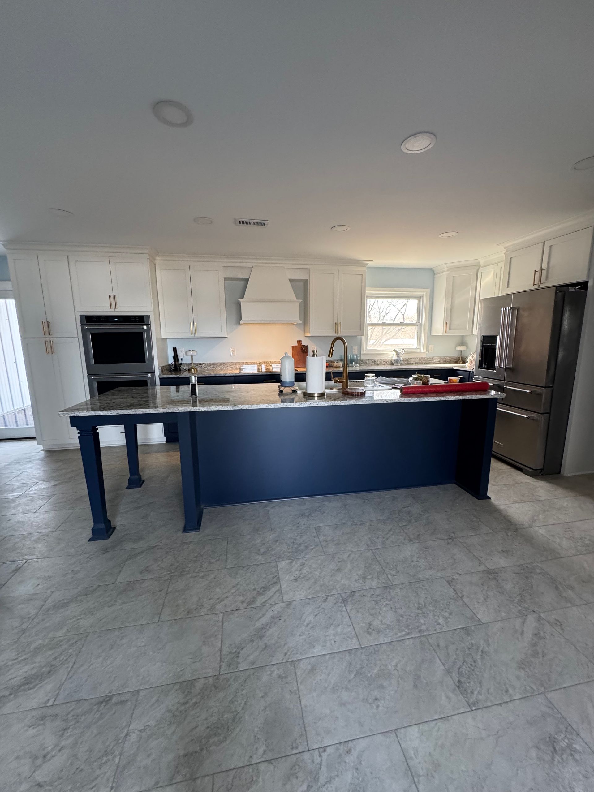 Kitchen with white cabinets, blue island, stainless steel appliances, and gray flooring.
