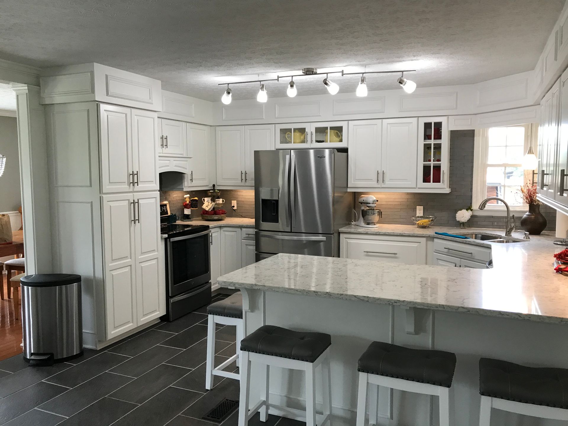 White kitchen with island seating, stainless steel appliances, and dark tile floor.