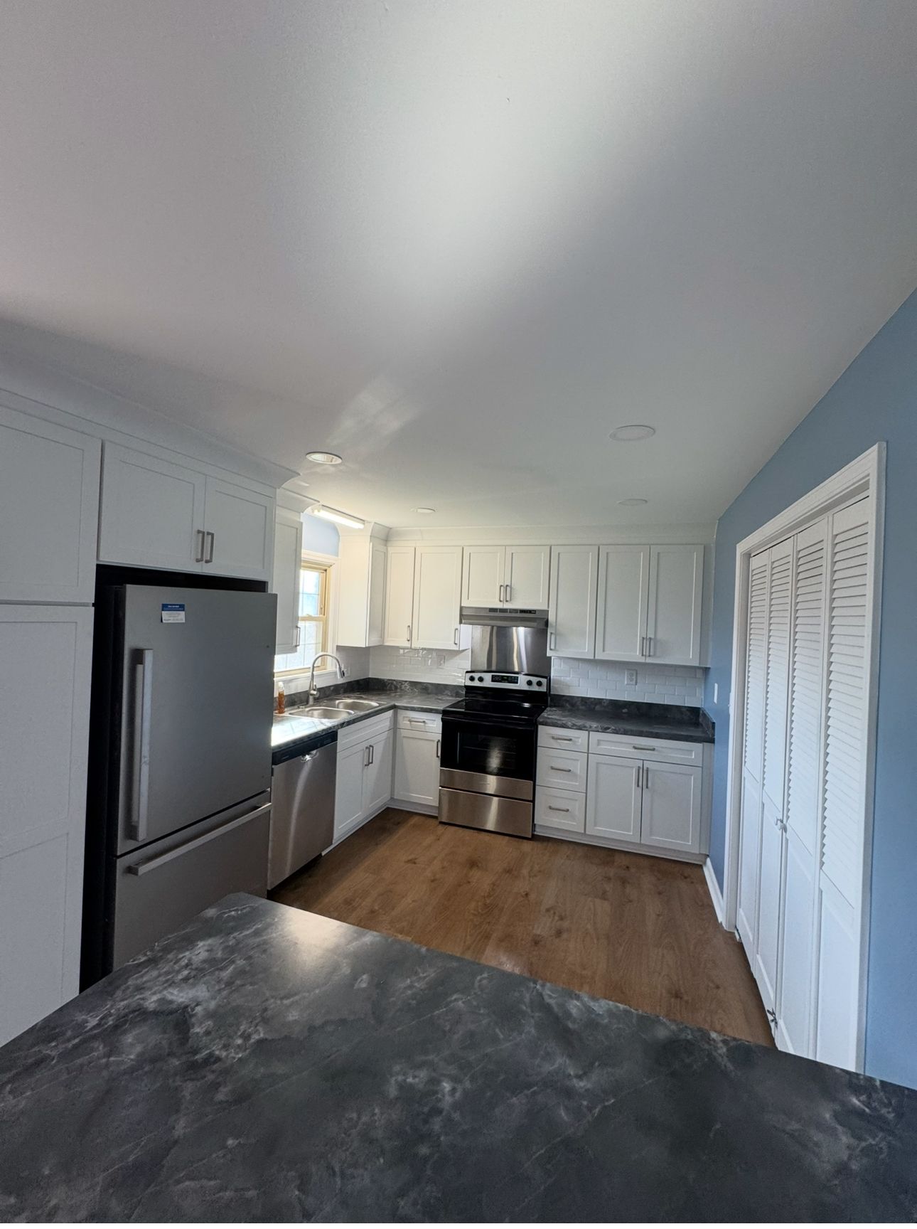 Modern kitchen with white cabinets, stainless steel appliances, and blue walls.