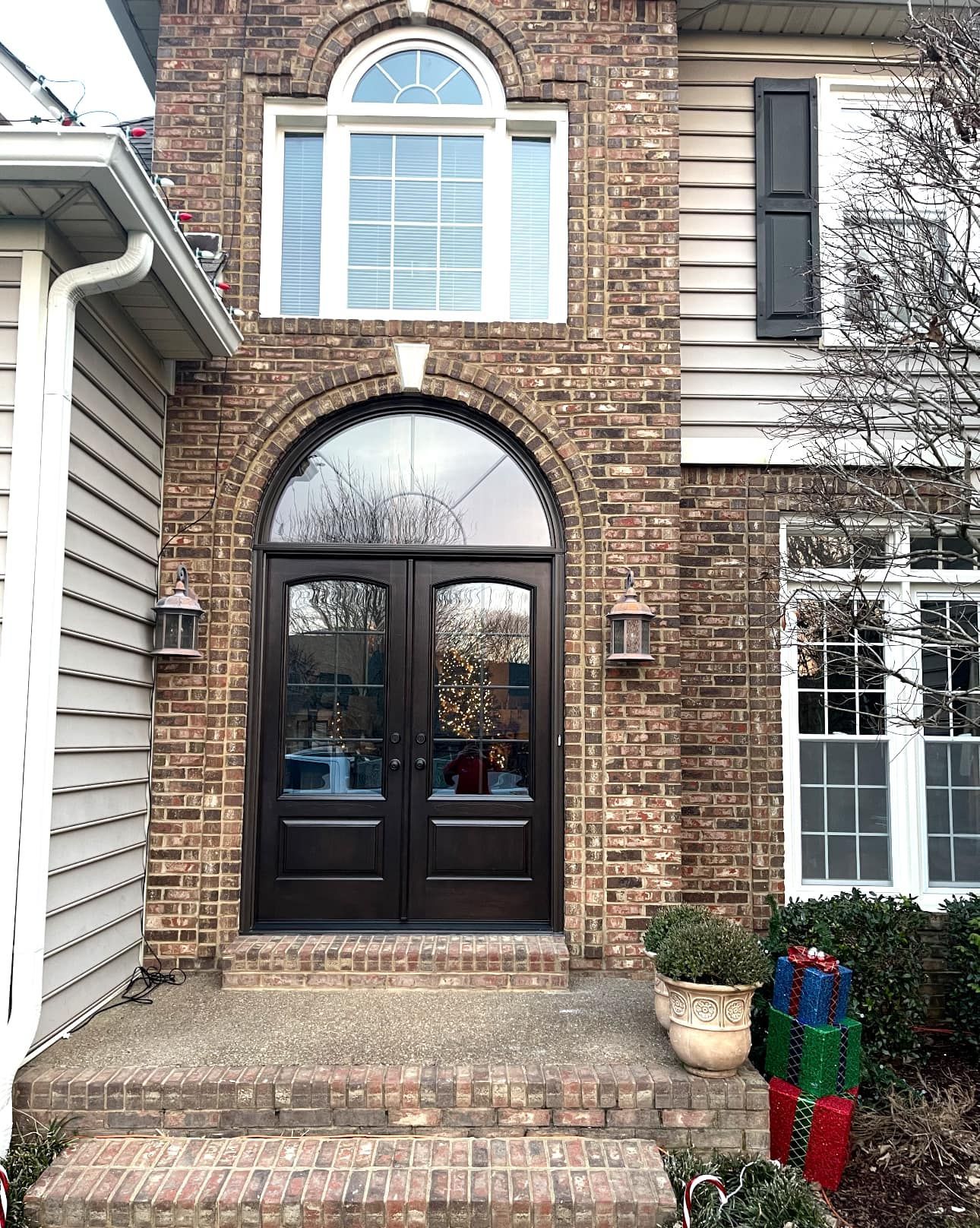 Brown brick home with arched front door and sidelight. Christmas decorations are visible.