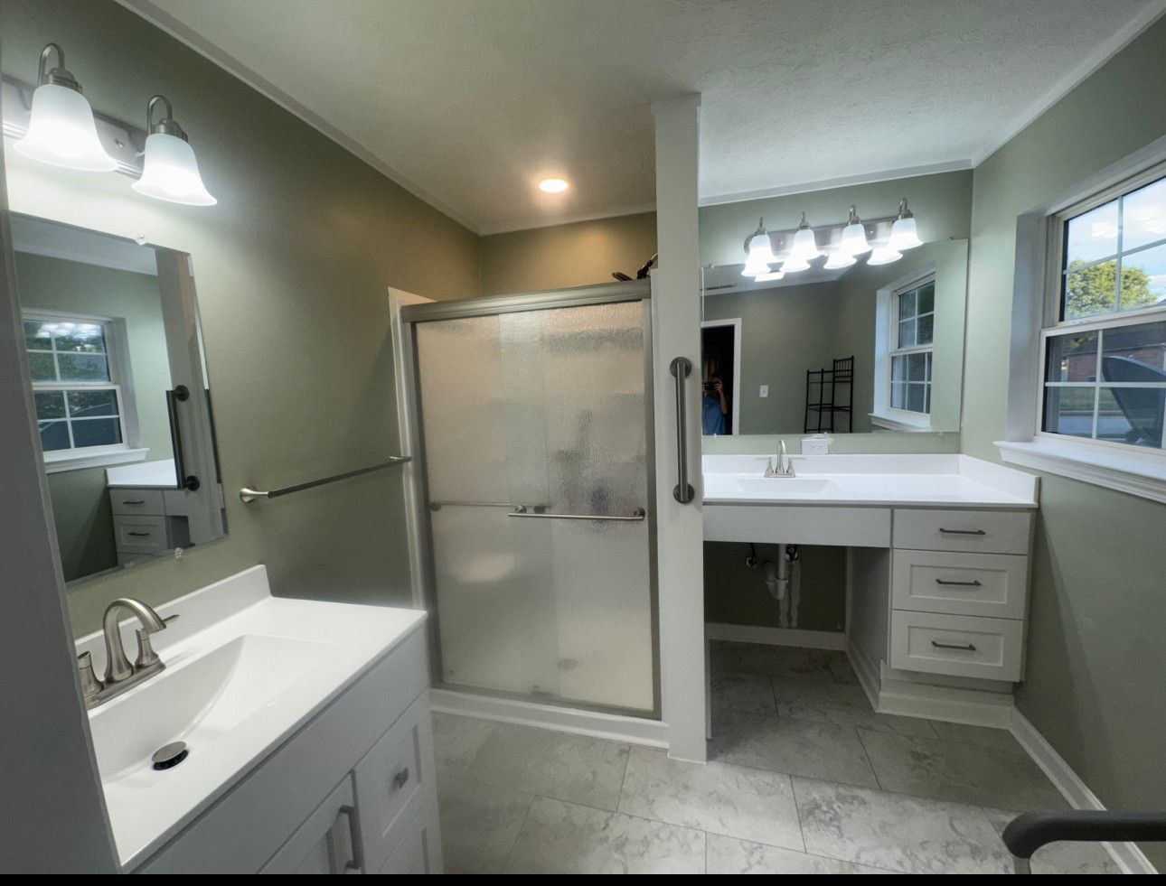 Bathroom with accessible features: shower, two sinks with grab bars, white cabinetry, pale green walls.