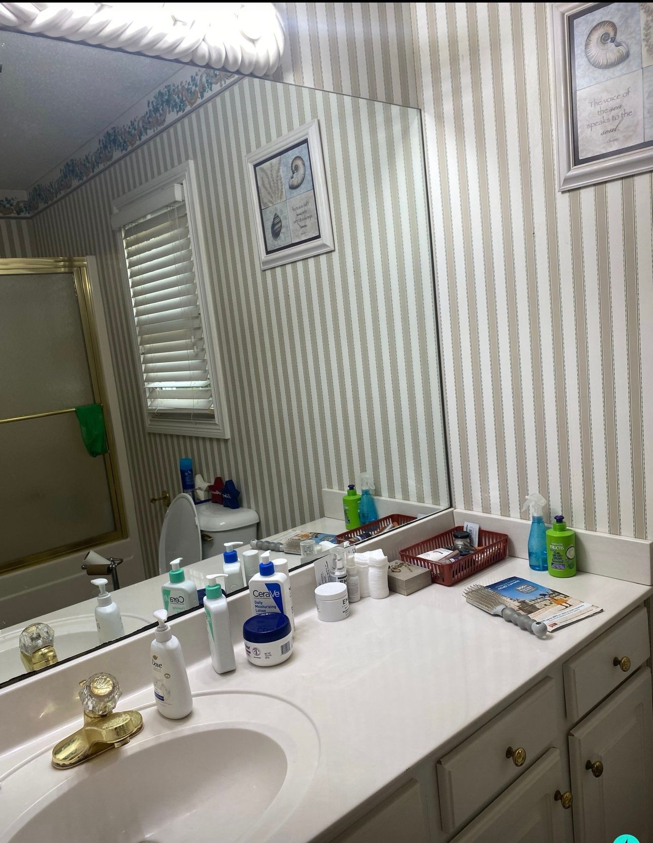 Bathroom with striped wallpaper, large mirror, and vanity with toiletries.