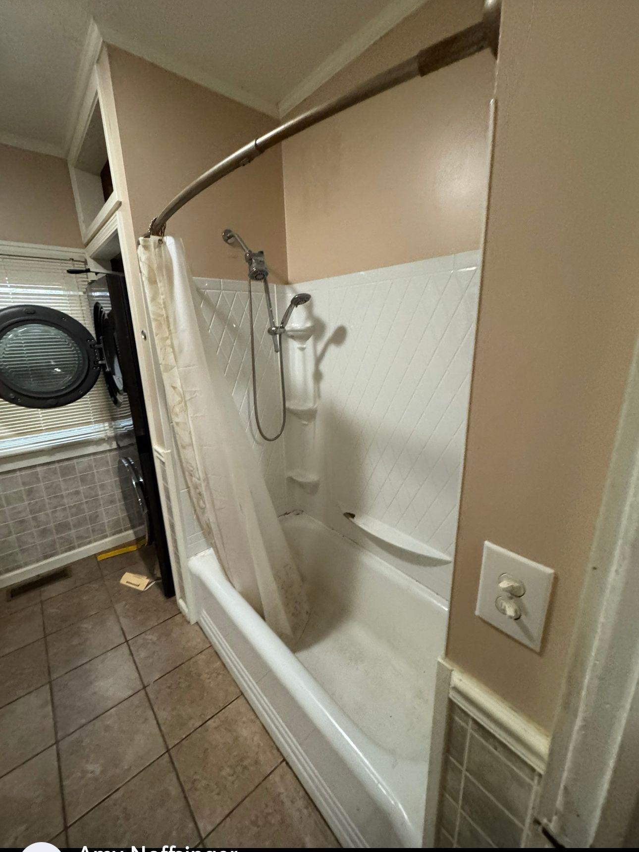 Bathroom with a white tub, showerhead, and a beige shower curtain. Beige and white walls, with brown tile flooring.
