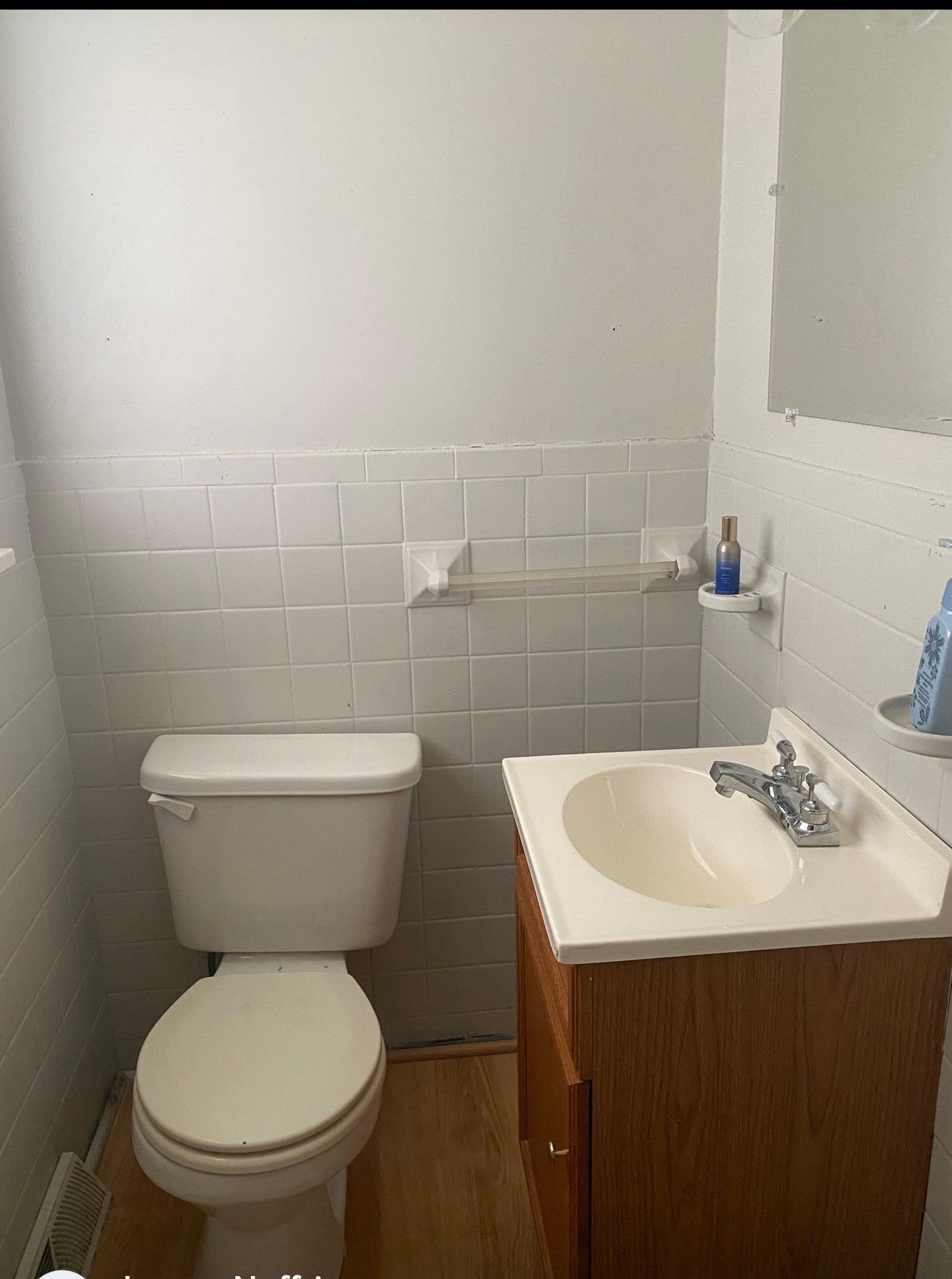 Small bathroom with white tiled walls, toilet, vanity, and mirror.